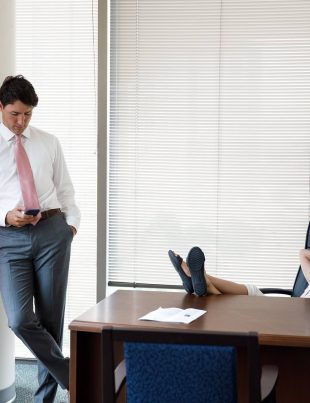 Justin Trudeau Standing Looking At Mobile Phone With Daughter Sitting At his Desk With Feet On Table