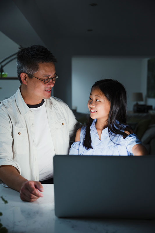 Smiling Asian Father Helping Young Daughter With A Computer