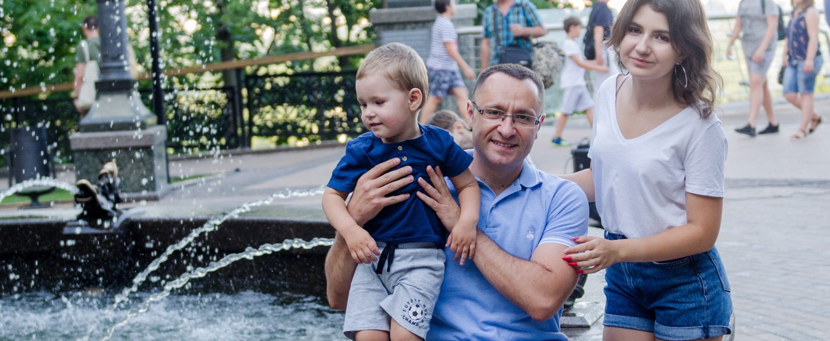 Vasyl Myroshnychenko Sitting By Fountain Holding Son In his Hands With Daughter Beside Him