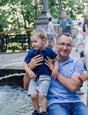 Vasyl Myroshnychenko Sitting By Fountain Holding Son In his Hands With Daughter Beside Him
