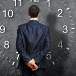 Man Looking At Giant Clock With His Back To Facing Us