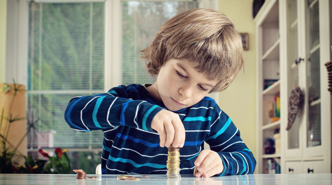 Young Boy Concentrating While Counting Stack Of Coins Credit: iStock