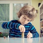 Young Boy Concentrating While Counting Stack Of Coins Credit: iStock