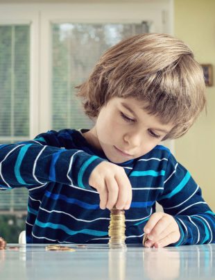 Young Boy Concentrating While Counting Stack Of Coins Credit: iStock