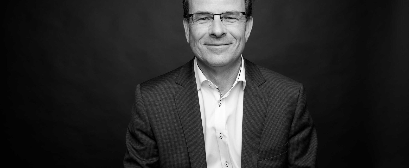 Black And White Corporate Style Head Shot Photo Of John Boynton Smiling
