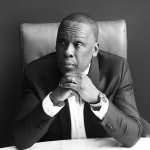Black And White Photo Of Bruny Surin Sitting Down With Both Hands Under His Chin