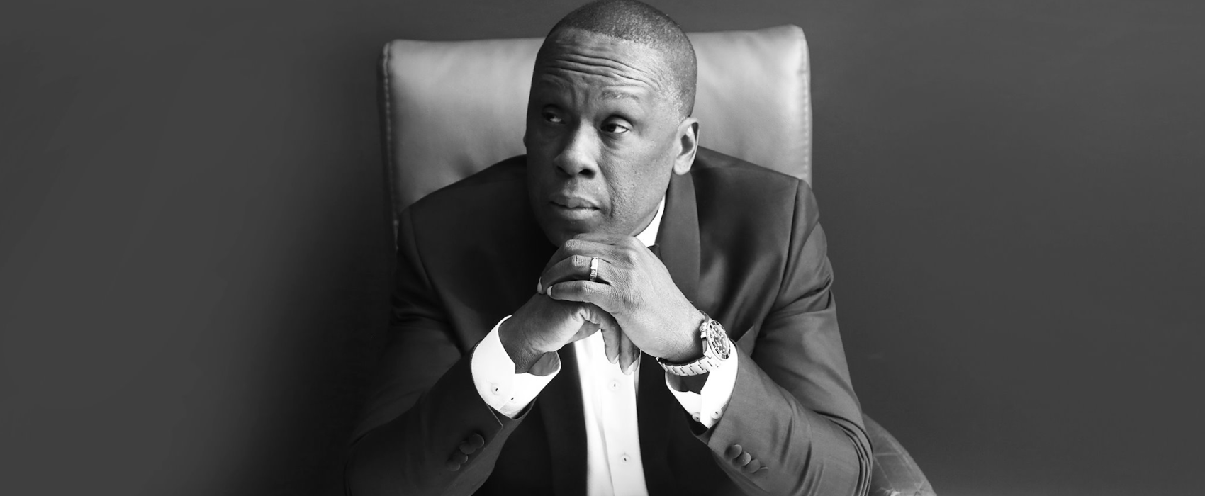 Black And White Photo Of Bruny Surin Sitting Down With Both Hands Under His Chin