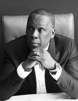 Black And White Photo Of Bruny Surin Sitting Down With Both Hands Under His Chin